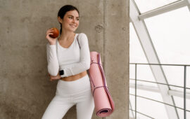 Young smiling woman holding yoga mat while standing with yoga mat indoors