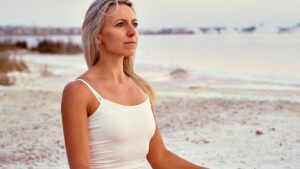 Kobieta medytująca na plaży - zdjęcie ilustracyjne we wpisie bloga Namaste24.pl "Sport, kobieta, menopauza"
